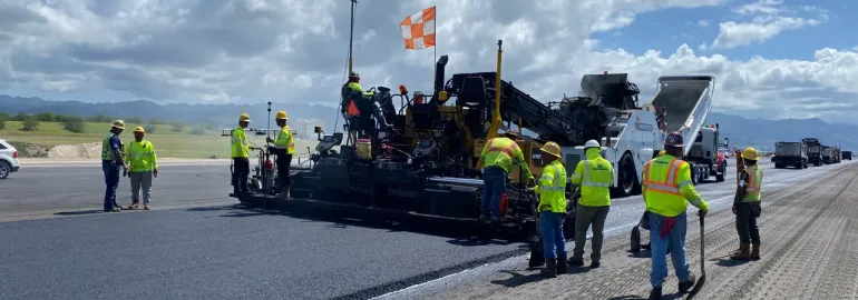 Runway 8L paving crew working beside an asphalt paver in daylight.